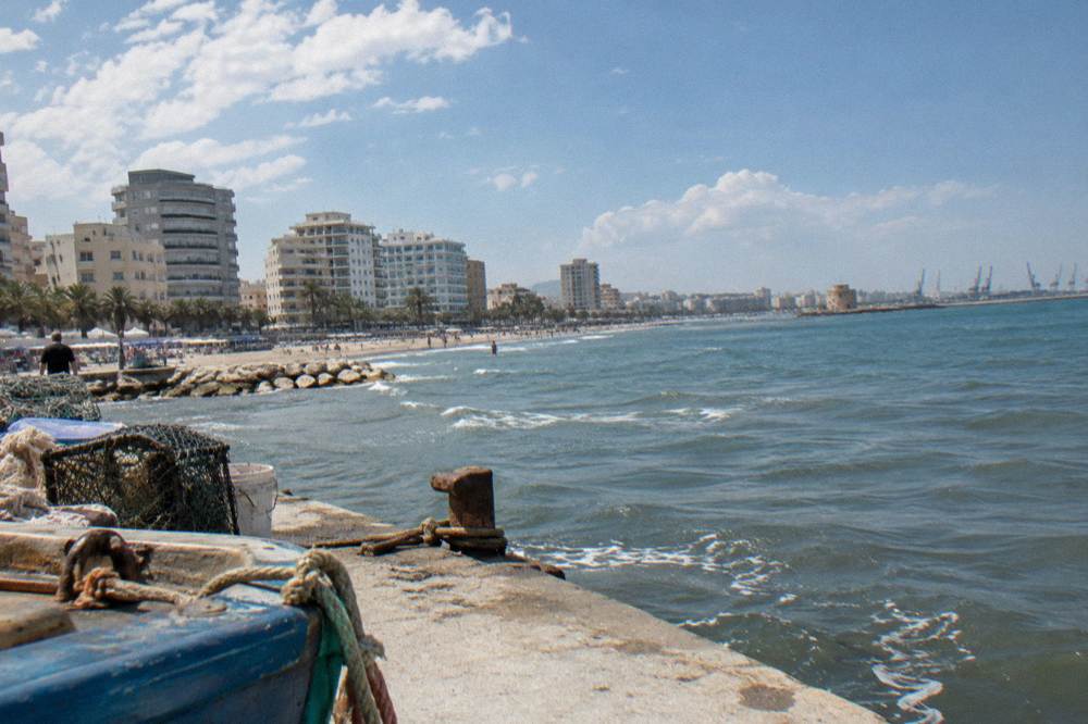 A port city on the Adriatic with a long sandy beach promenade, mid-rise hotels, palm trees and a calm blue sea with low swell